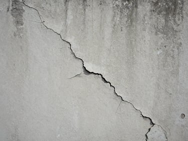 Close-up of a cracked concrete wall with peeling paint, flat overcast light, no people, showing deterioration clearly at arm's length