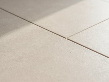Extreme close-up of seamless joints in a cold-pressed porcelain tile floor, natural side-light casting soft shadows, warm neutral tones