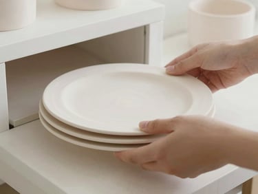 Close-up of a person neatly placing white raw ceramic plates onto a kiln shelf, soft daylight, minimalist setting, 35mm