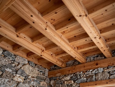 Interior view of a remodeled mountain cabin ceiling, exposed rough-hewn pine rafters meeting a natural stone wall.