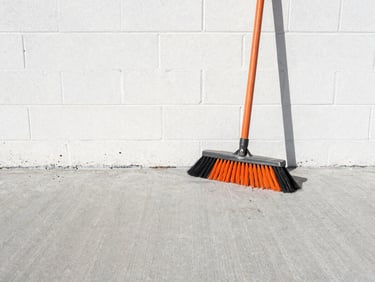A spotless concrete floor after cleanup, industrial broom resting against a pristine brick wall, high-contrast, sharp focus.