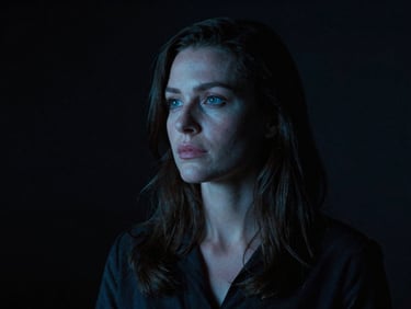 Cinematic portrait of a female film director in a dark studio, soft blue screen glow on her face, thoughtful expression, anamorphic lens, high-contrast.