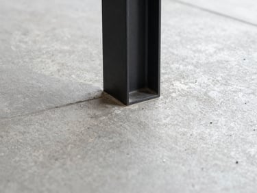Macro straight-on detail shot of a premium material junction, polished concrete meeting a matte black steel column, soft diffused daylight, sharp focus.