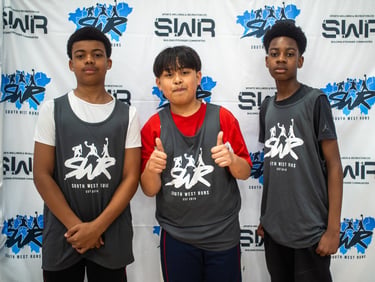 Three young basketball players in SWR South West Runs jerseys posing at a sports community event.