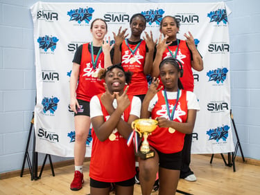 A youth girls basketball team in red jerseys posing with a trophy and medals at an SWR tournament.