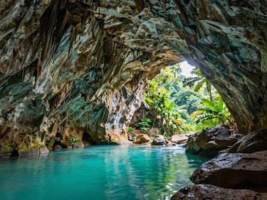Interior de una cueva de piedra caliza con un manantial de agua cristalina turquesa, reflejos de luz natural en las paredes arqueadas.