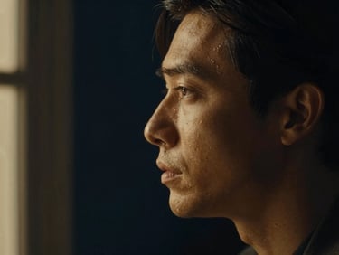 Low-key dramatic portrait of an actor in profile, illuminated by warm window light against a deep navy background, rich chiaroscuro.