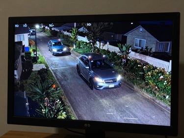 Close-up of a monitor screen displaying sharp HD security footage of a driveway at night, faces and licence plates clearly readable in the night-vision frame, studio lighting on the screen to emphasize image clarity