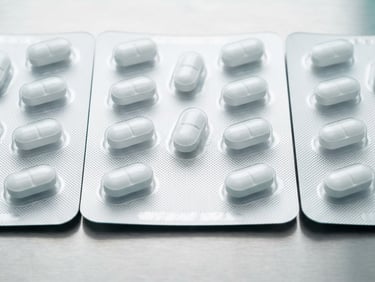 Macro shot of sealed pharmaceutical blister packs on a sterile steel surface, bright high-key clinical white light, sharp focus