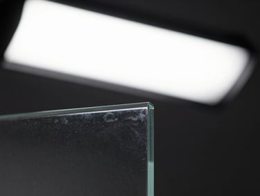 Close-up of a clear glass panel edge under bright studio strobe lighting, showing full transparency and slight reflective surface, 1/2-inch thickness visible at the cut edge