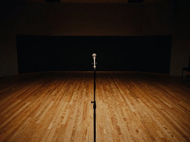 Wide environmental shot of an empty live recording room, low-key lighting, deep shadows, with a microphone stand in the foreground.