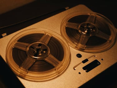 Close-up of a spinning reel-to-reel tape machine, low-key lighting, warm amber glow, 35mm film grain