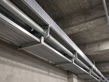 Wide-angle structural shot of neatly organized heavy-duty cable trays and electrical conduits along a concrete ceiling