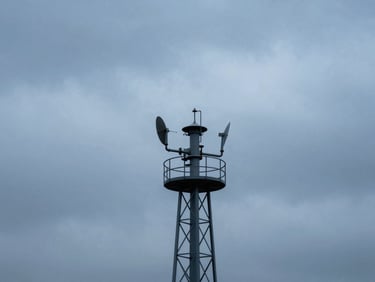 An industrial air quality monitoring tower silhouetted against a dramatic, cool-toned overcast sky, architectural framing.