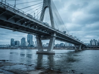 Wide environmental shot of a modern highway bridge crossing a river, shot from a low architectural angle, cool overcast daylight, desaturated steel blue tones.