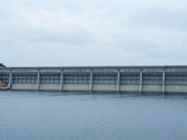 Wide environmental shot of a massive, structurally engineered water containment reservoir and tailings dam, overcast sky.