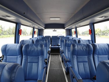 Interior wide-angle shot of a luxury passenger coach showing clean blue upholstery, spacious legroom, and bright natural window light.