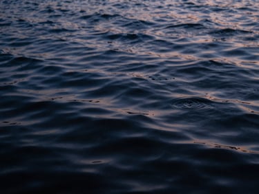 Close-up of rippling water surface at dusk, deep indigo and slate tones, moody film photography, shallow depth of field.