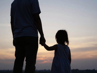 Warm silhouette of a father holding a young daughter's hand against a golden hour sky, shallow depth of field, atmospheric, low horizon.