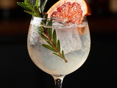 An elegant gin tonic garnished with botanicals and a slice of grapefruit. Light, airy but sophisticated, high-contrast, editorial photography.