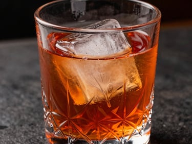 A close-up of a negroni with a stamped clear ice cube inside a heavy crystal glass. Moody shadows, rich orange and amber tones, luxury bar setting in Brazil.