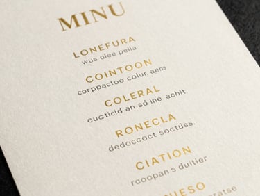 A minimalist design of a cocktail menu showing golden text on a clean, premium off-white paper. Editorial layout.