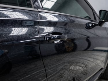 Close-up before-and-after of deep scratches on a black metallic car door, transitioning to a flawless mirror-like clear coat reflecting overhead LED bar lights