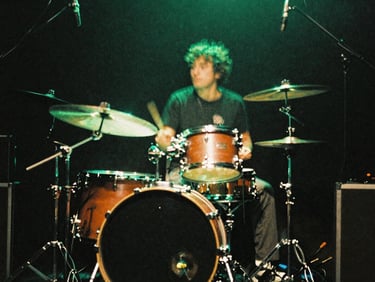 Gritty, motion-blurred shot of a drum kit on a dark stage under electric neon green lighting flares, 35mm film.