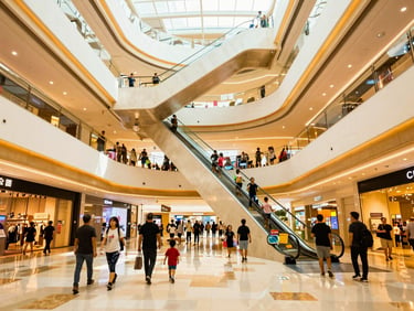 Interior photo of a bustling modern shopping mall atrium with multiple floors, escalators, and families shopping under warm natural atrium light, vibrant atmosphere.