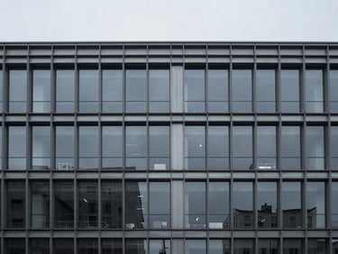 Wide environmental architectural shot of a minimalist corporate office building exterior, cool overcast daylight, desaturated slate and steel tones, 35mm lens