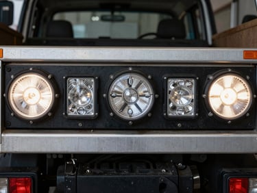 Close-up of bright LED safety lights installed on the rear of a commercial utility truck, workshop background blurred, gritty metallic tones.
