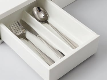 Overhead flat lay of neatly arranged kitchen drawer dividers holding stainless steel utensils, bright high-key lighting, soft gray background