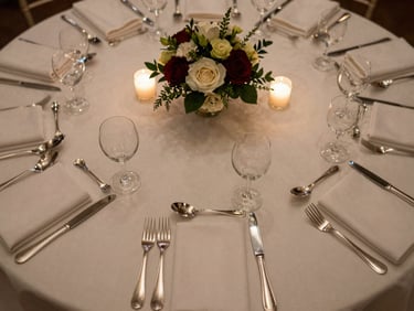 Overhead close-up of a hotel banquet table in final dress — folded napkins, polished silverware, floral centerpiece, candlelight warmth, no guests, shot from directly above