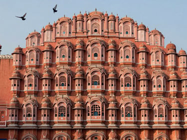 Hawa Mahal's pink sandstone facade in Jaipur photographed from street level at early morning, warm backlight catching the latticed windows, a few pigeons in flight at the upper edge of the frame