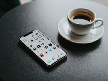 Overhead view of a phone resting on a café table beside an empty espresso cup, app grid visible on screen, soft diffused afternoon light, sparse and unhurried composition
