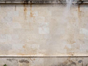 Wide shot of a Corsican stone façade after steam cleaning, soft overcast daylight, clean pale limestone texture restored, no algae remaining, subtle moisture still visible on the surface