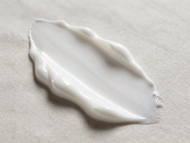 Macro shot of a rich, velvety white facial cream texture being gently smoothed over a soft linen surface