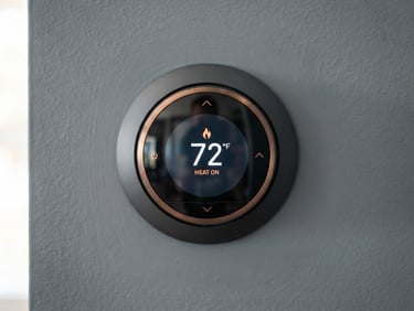 Straight-on macro photograph of a modern digital thermostat mounted on a clean slate gray wall, bright natural daylight, technical precision, shallow depth of field.