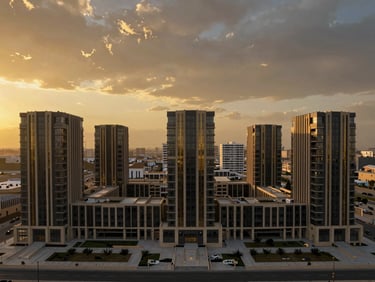 Sweeping cinematic drone shot of a new development in Fallujah, capturing modern architecture under a dramatic golden-hour sky, symmetrical framing, subtle gold accents, wide-angle heroic perspective.