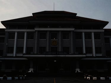 Wide shot of a dark Indonesian government building facade at dusk, dramatic lighting, high-contrast, deep shadows