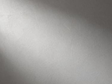Macro detail of freshly applied gypsum plaster surface showing uniform texture and smooth finish on a completed interior wall, controlled studio strobe lighting raking across the surface to reveal flatness