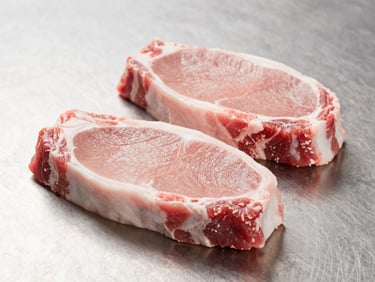 Fresh raw pork chops on a stainless steel surface, bright processing room lighting, crisp details