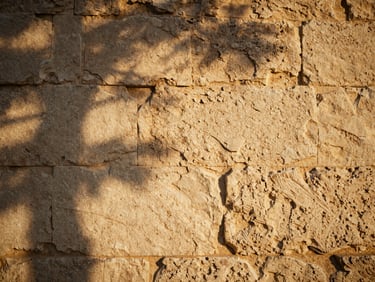 A close-up of sun-drenched ancient stone walls with soft shadow patterns, warm editorial photography, golden-hour natural light.