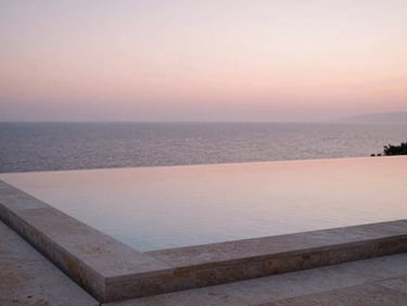 An empty stone infinity pool reflecting the soft pink dawn light over the Adriatic sea, minimalist luxury, quiet atmosphere.