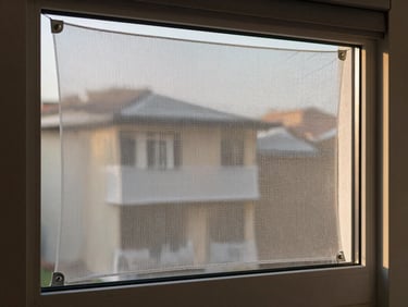 Close-up of a taut protection net stretched across a residential window frame, fine UV-resistant mesh catching soft morning light, clean aluminum fixings at the corners, interior wall visible behind