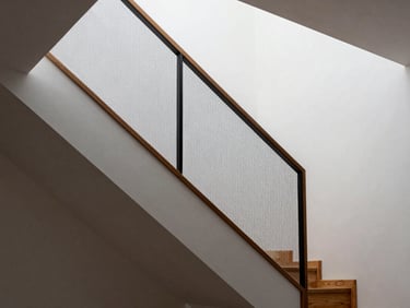 Interior staircase of a modern home with a fine vertical safety net panel installed along the open side, white walls and wooden steps, natural light from above, net integrated cleanly into the railing structure
