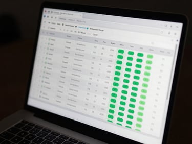 A clean dashboard interface of an attendance tracker on a laptop screen, showing database tables and green status chips, angled side view.