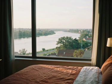 Top floor homestay room with wide river view from window, golden hour light, cozy bed, brass accents, shallow depth of field, 35mm film