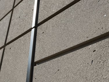 Close-up of textured ash plaster panels with embedded cold-rolled steel accents, low-angle raking light showing deep tactile details.