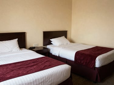 Wide shot of a large hotel room with two double beds, neat presentation, warm cream walls